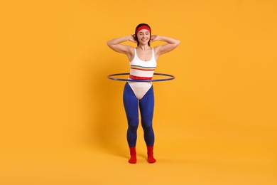 Photo of Smiling woman training with hula hoop on orange background