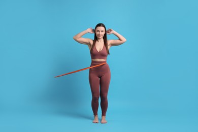 Photo of Beautiful woman training with hula hoop on light blue background