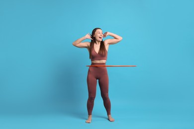 Photo of Happy woman training with hula hoop on light blue background