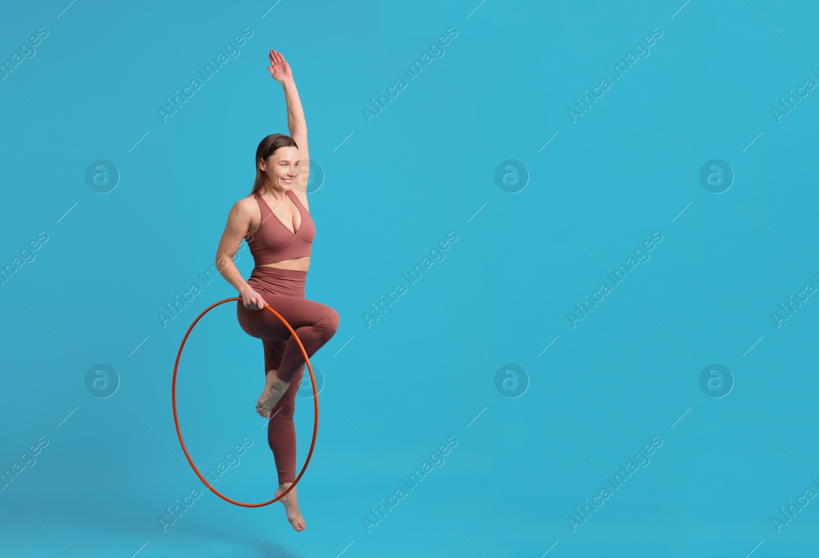 Photo of Smiling woman jumping with hula hoop on light blue background. Space for text