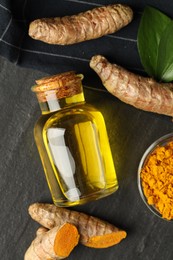 Photo of Tumeric oil, powder and roots on black table, flat lay