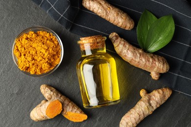 Photo of Tumeric oil, powder and roots on black table, flat lay