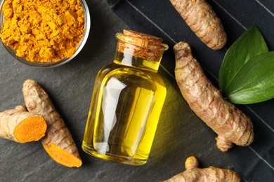 Photo of Tumeric oil, powder and roots on black table, flat lay