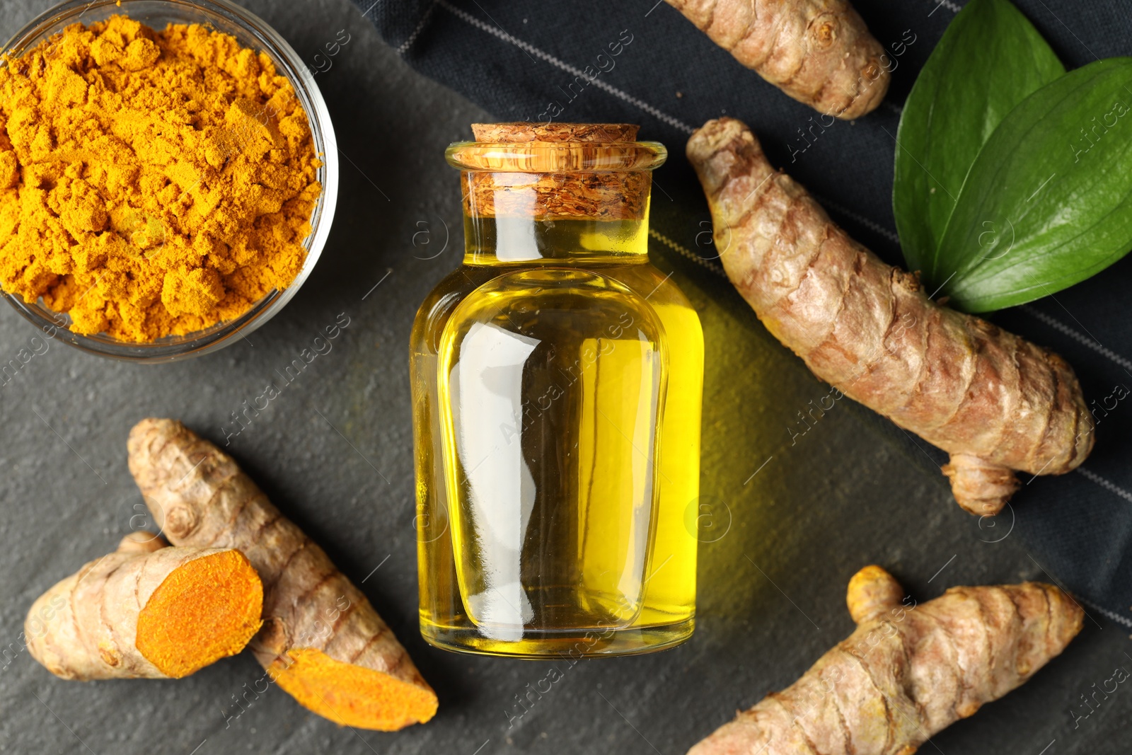 Photo of Tumeric oil, powder and roots on black table, flat lay