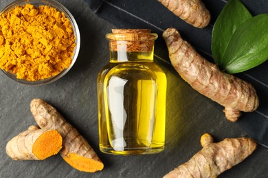 Photo of Tumeric oil, powder and roots on black table, flat lay