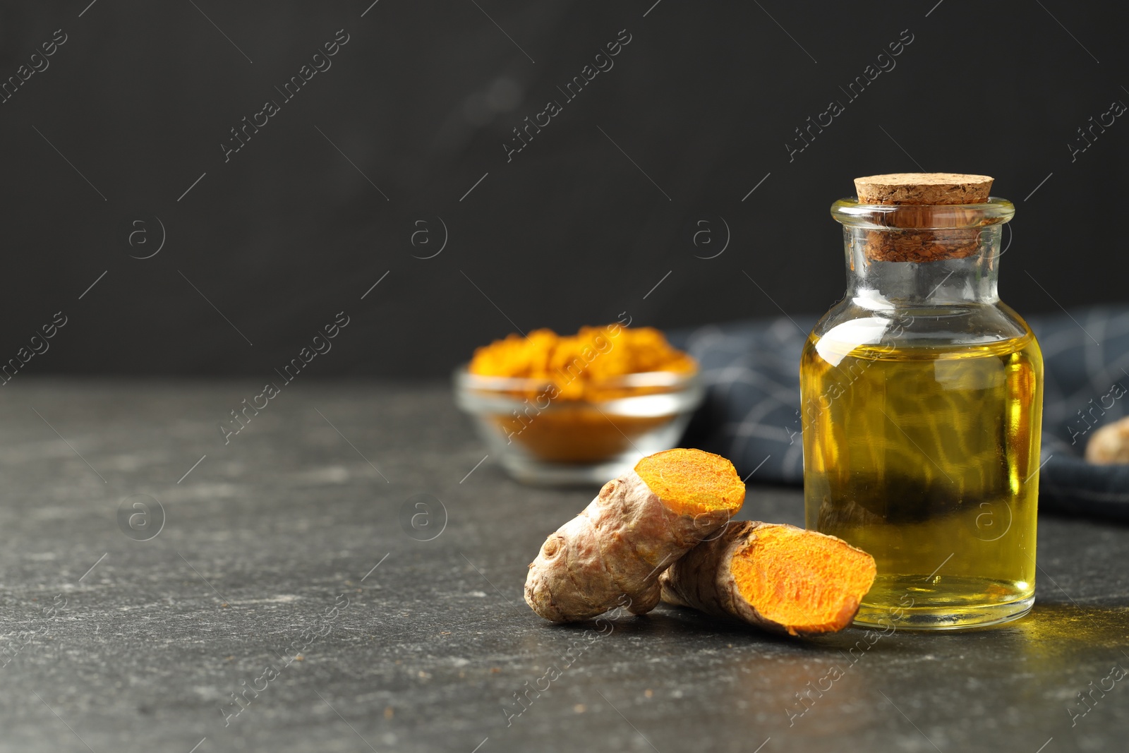 Photo of Tumeric oil and roots on black table, closeup. Space for text