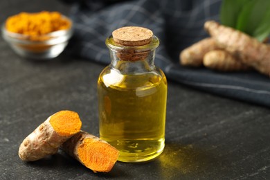 Photo of Tumeric oil and roots on black table, closeup