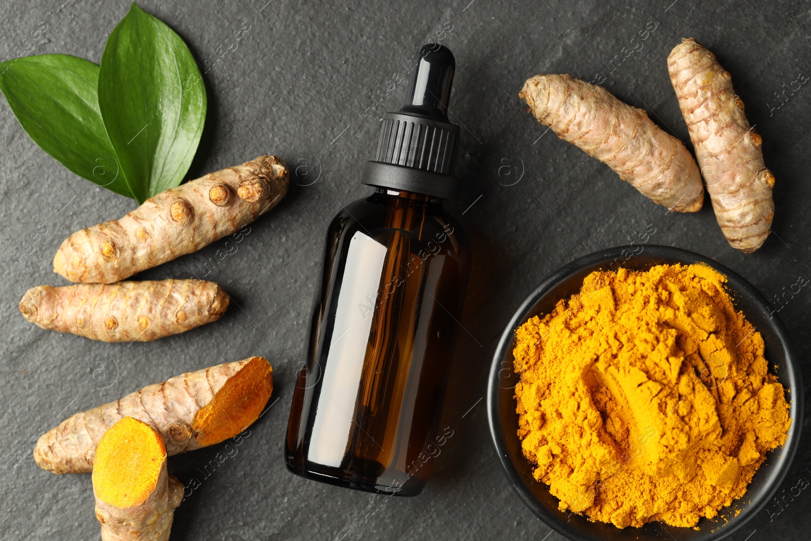 Photo of Tumeric oil, powder and roots on black table, flat lay