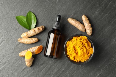 Photo of Tumeric oil, powder and roots on black table, flat lay