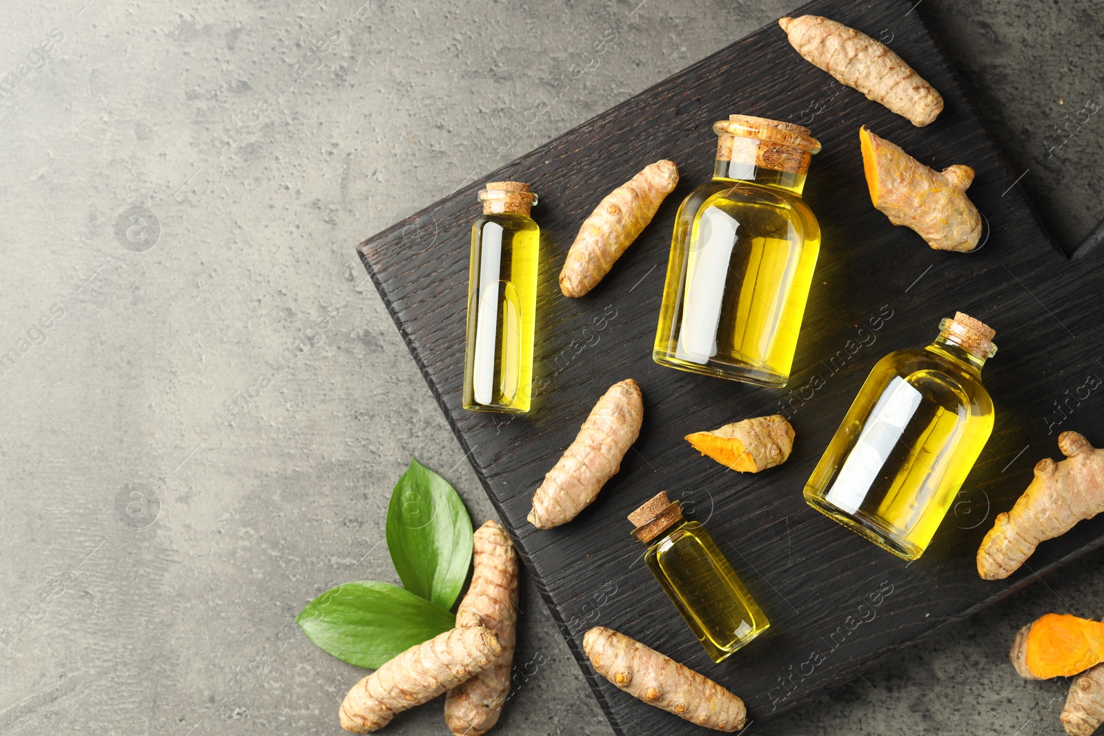 Photo of Tumeric oil and roots on grey table, flat lay. Space for text