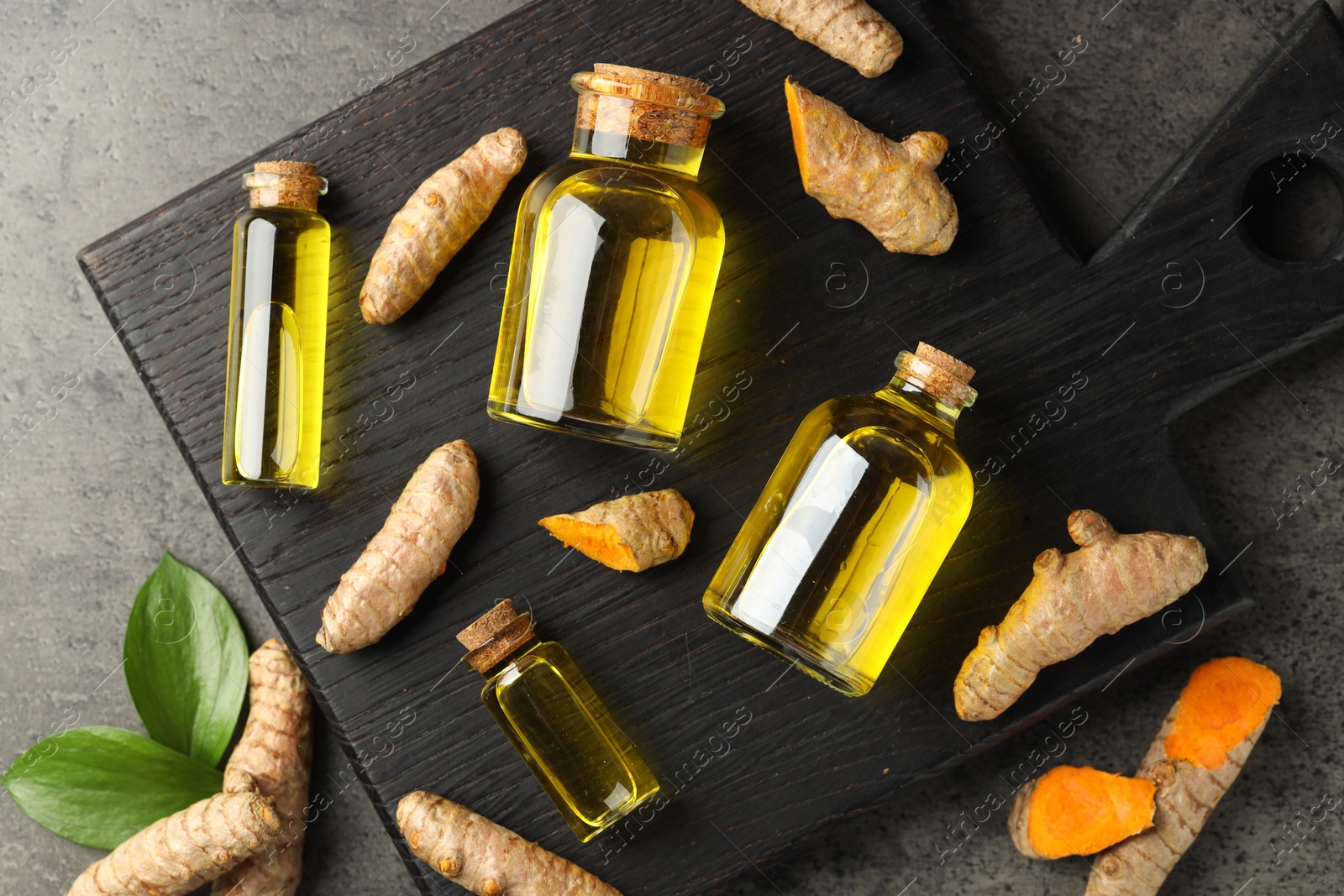 Photo of Tumeric oil and roots on grey table, flat lay