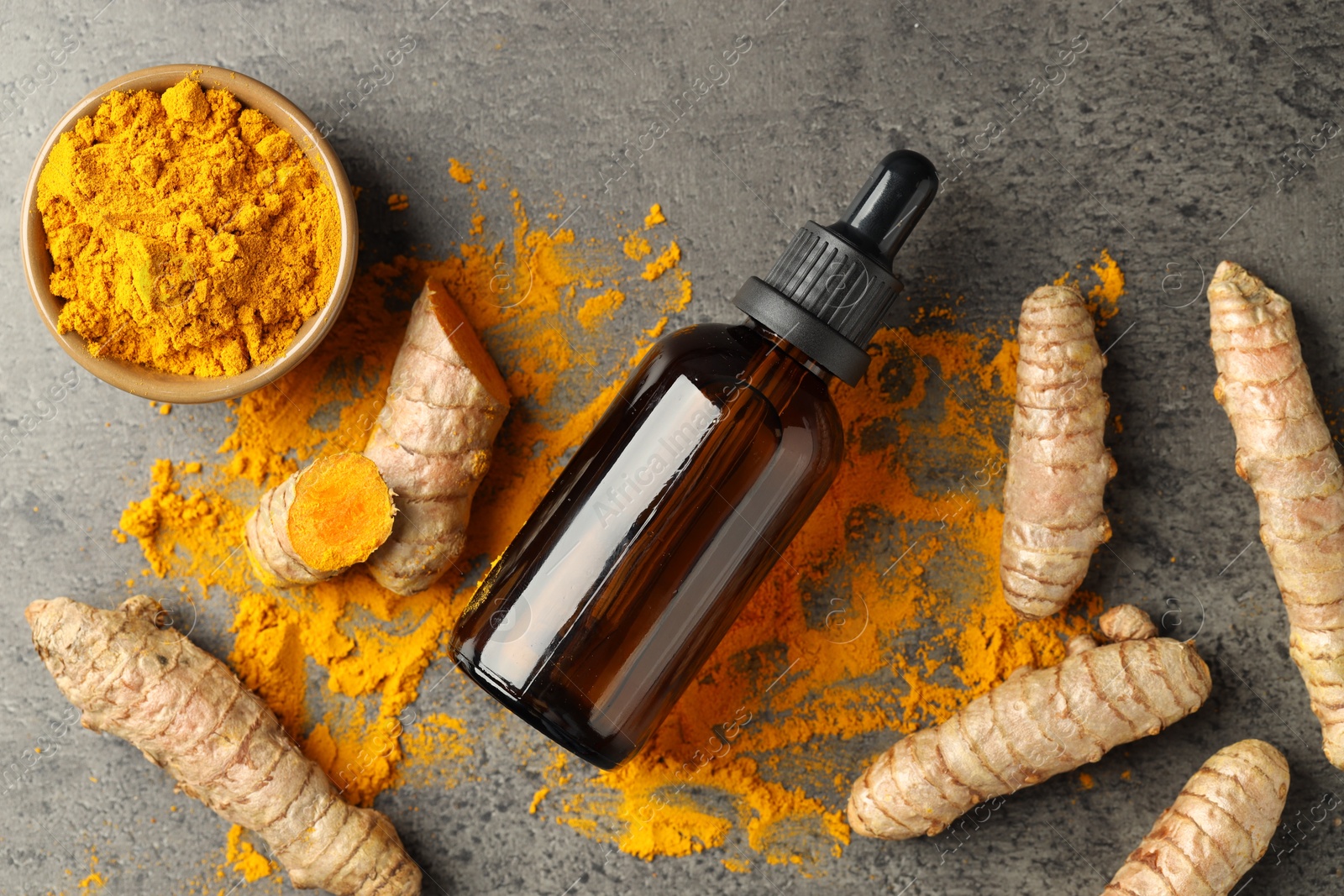 Photo of Tumeric oil, powder and roots on grey table, flat lay