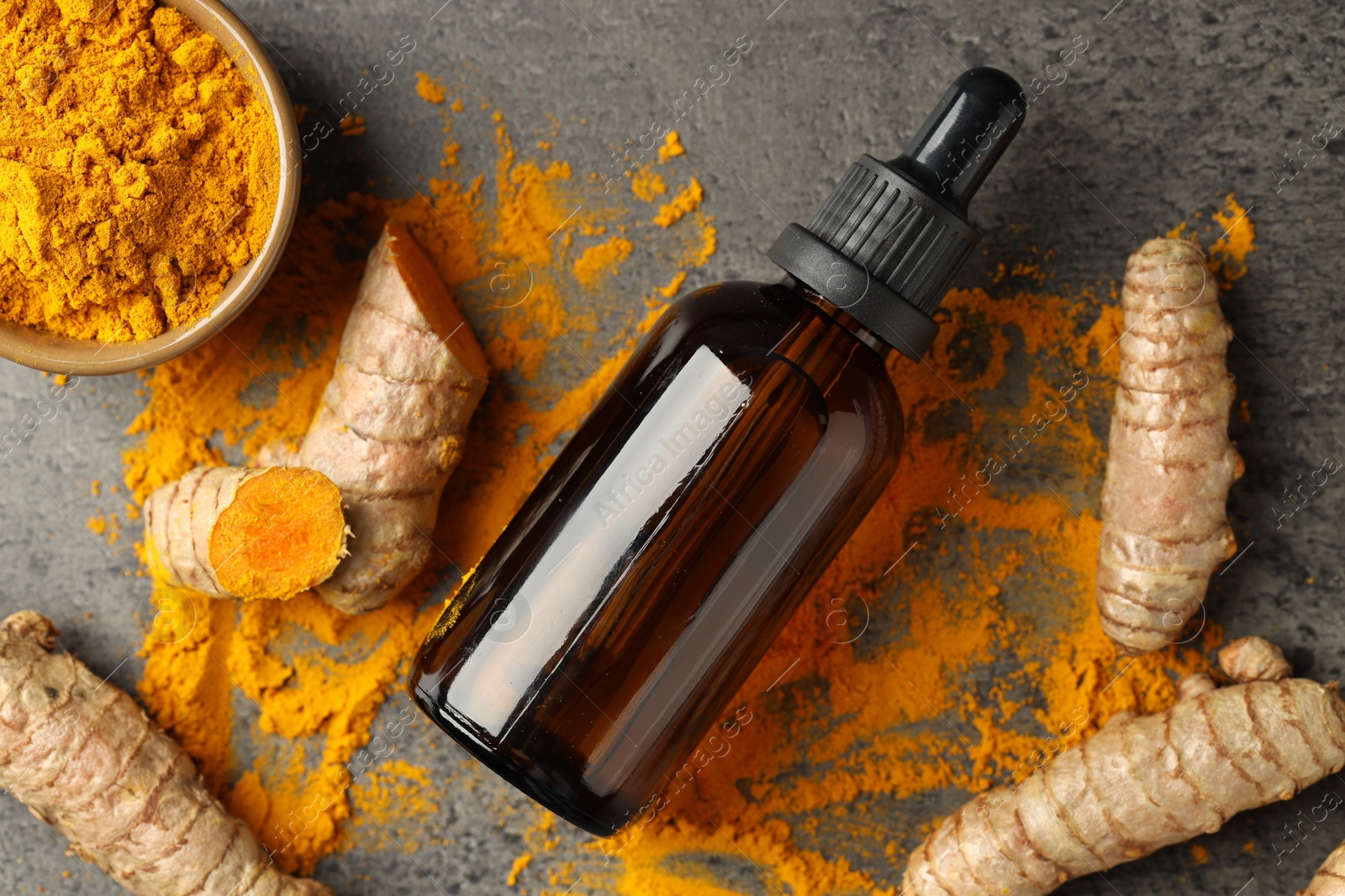 Photo of Tumeric oil, powder and roots on grey table, flat lay