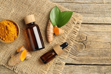 Photo of Tumeric oil, powder and roots on wooden table, flat lay