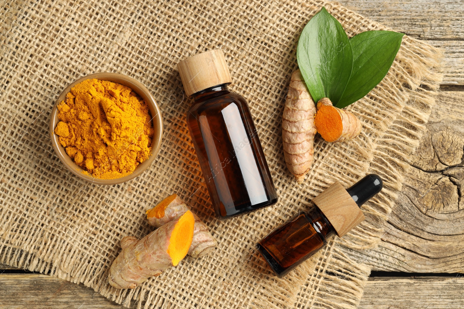 Photo of Tumeric oil, powder and roots on wooden table, flat lay