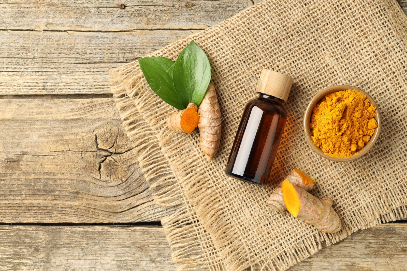 Photo of Tumeric oil, powder and roots on wooden table, flat lay. Space for text