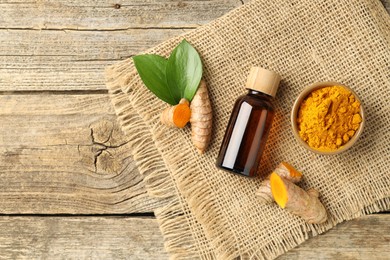 Photo of Tumeric oil, powder and roots on wooden table, flat lay. Space for text