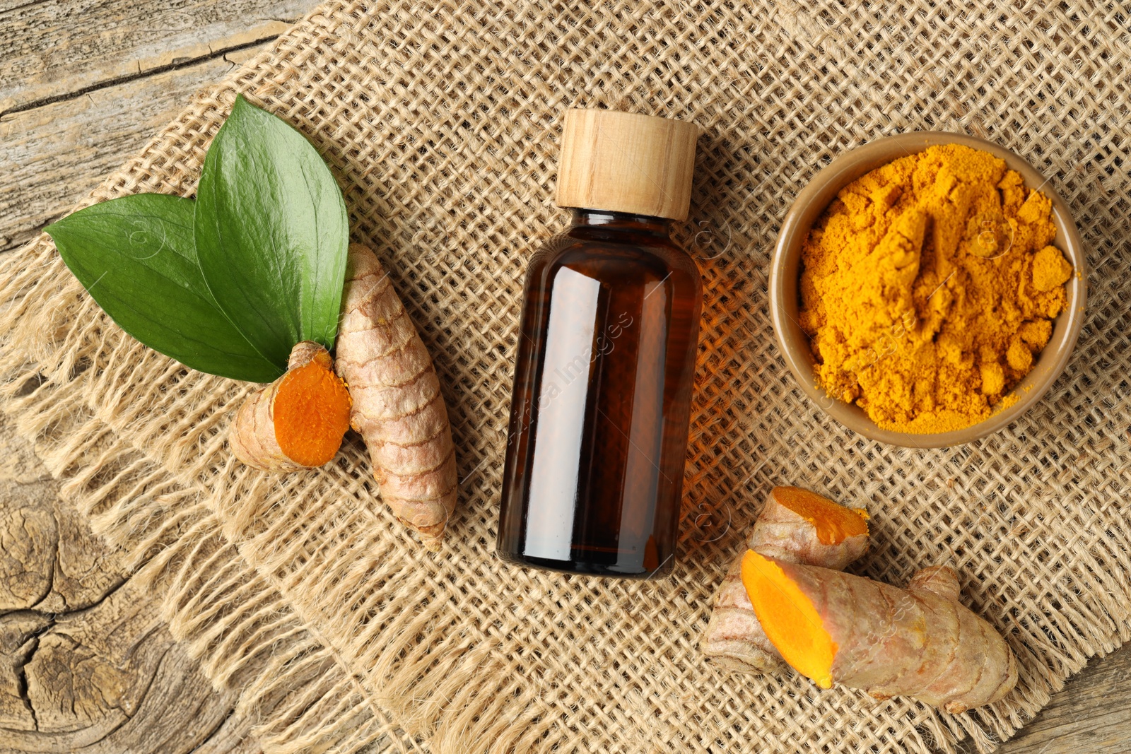 Photo of Tumeric oil, powder and roots on wooden table, flat lay