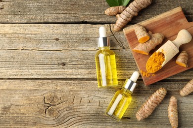 Photo of Tumeric oil, powder and roots on wooden table, flat lay. Space for text