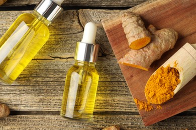 Photo of Tumeric oil, powder and roots on wooden table, flat lay