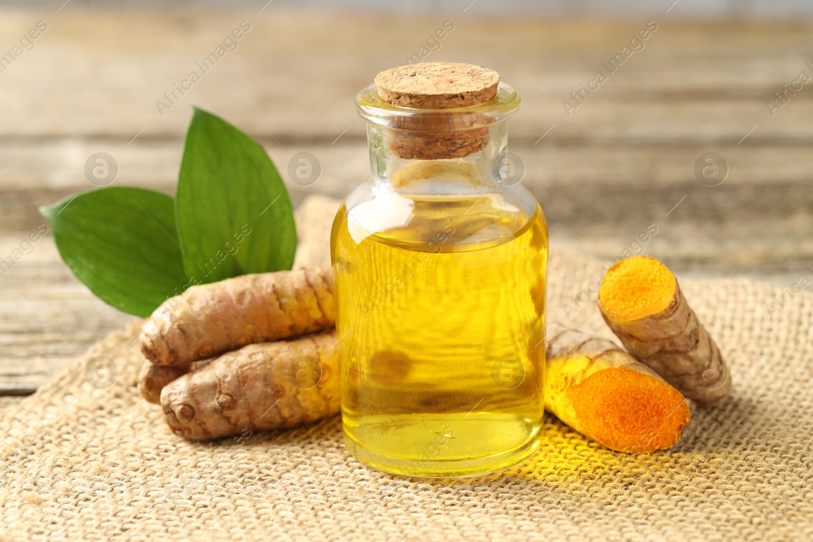 Photo of Tumeric oil and roots on wooden table, closeup