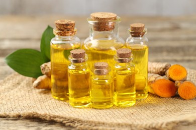 Photo of Tumeric oil and roots on wooden table, closeup