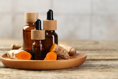 Photo of Tumeric oil and roots on wooden table, closeup. Space for text