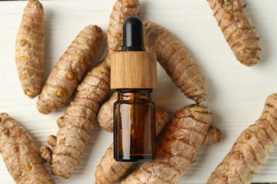 Photo of Tumeric oil and roots on white wooden table, flat lay