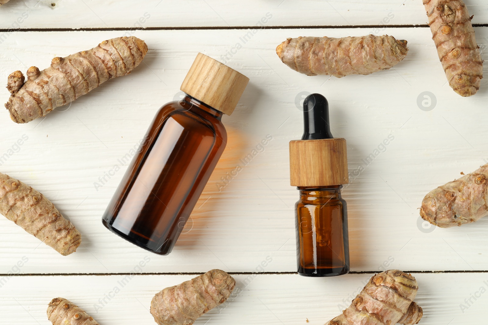 Photo of Tumeric oil and roots on white wooden table, flat lay