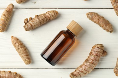 Photo of Tumeric oil and roots on white wooden table, flat lay