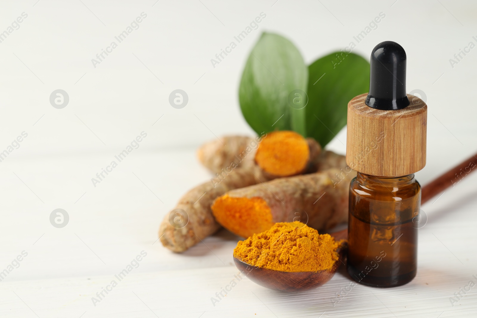 Photo of Tumeric oil, powder and roots on white table, closeup. Space for text