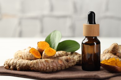 Photo of Tumeric oil, powder and roots on white table, closeup