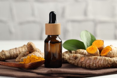 Photo of Tumeric oil, powder and roots on white table, closeup