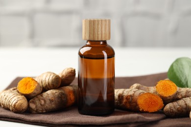 Photo of Tumeric oil and roots on white table, closeup