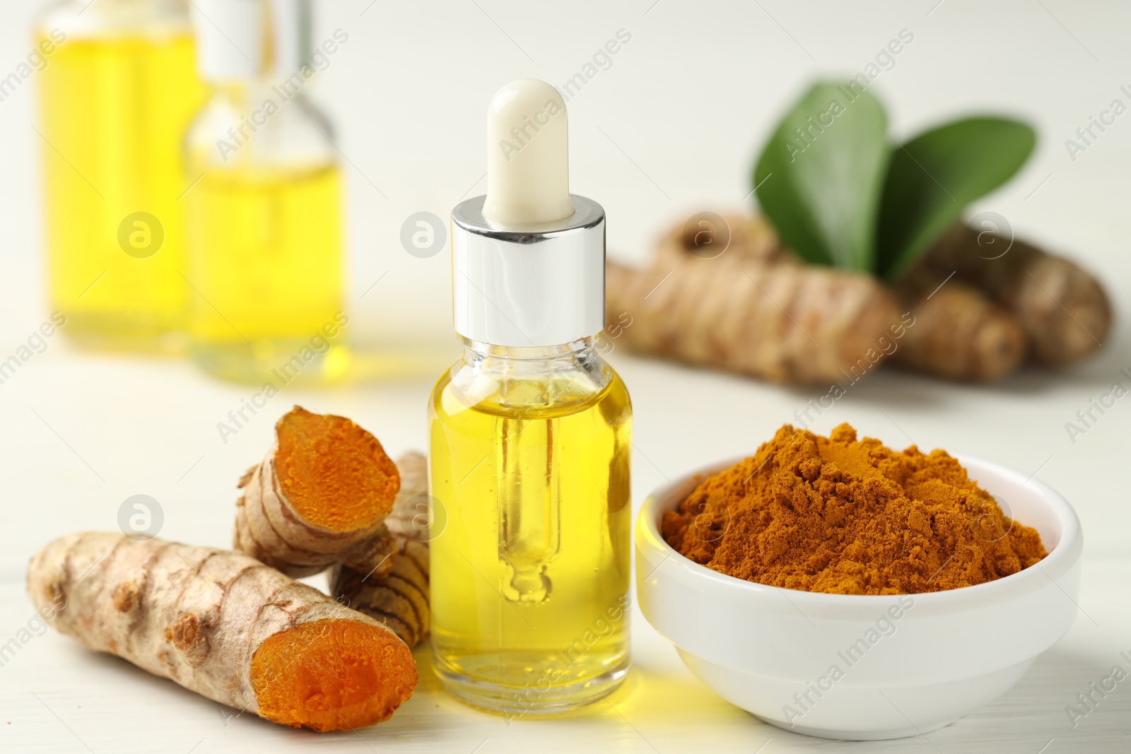 Photo of Tumeric oil, powder and roots on white table, closeup