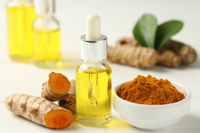 Photo of Tumeric oil, powder and roots on white table, closeup