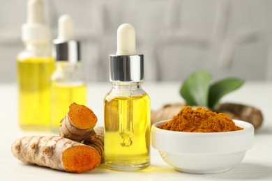 Photo of Tumeric oil, powder and roots on white table, closeup