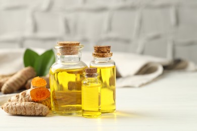 Photo of Tumeric oil and roots on white table, closeup. Space for text