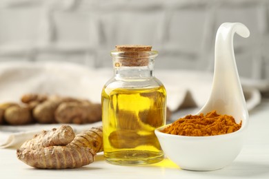 Photo of Tumeric oil, powder and roots on white table, closeup