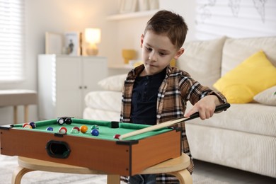 Photo of Cute little boy playing billiards at home