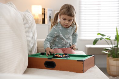 Photo of Cute little girl playing billiards at home