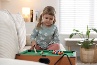 Photo of Cute little girl playing billiards at home