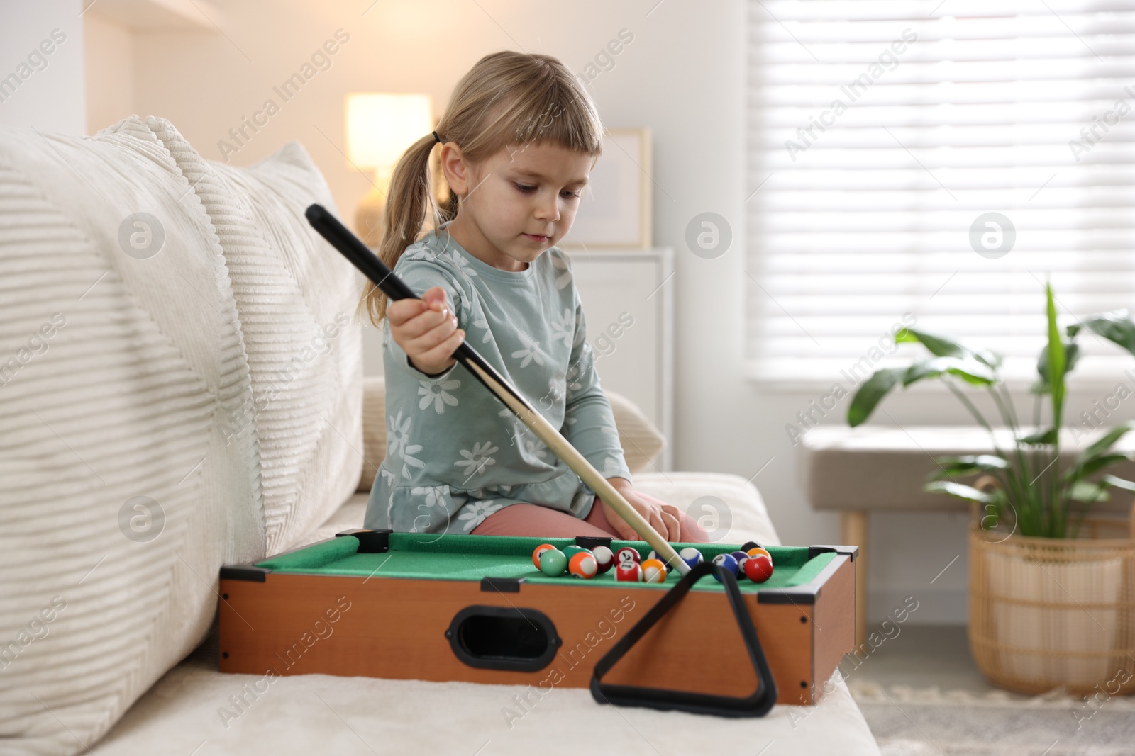 Photo of Cute little girl playing billiards at home