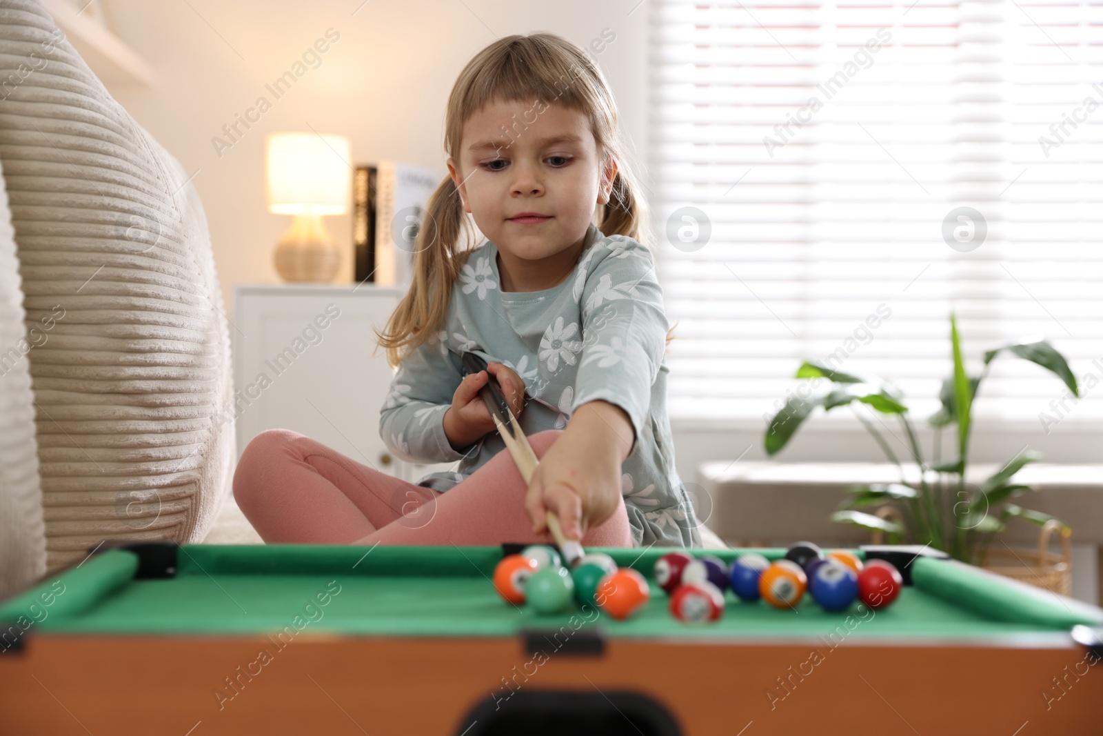 Photo of Cute little girl playing billiards at home