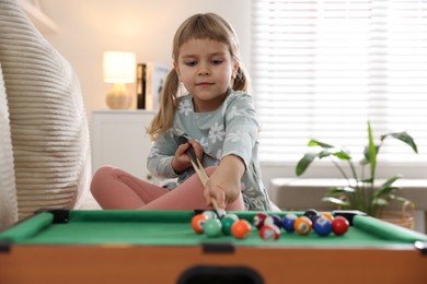 Photo of Cute little girl playing billiards at home