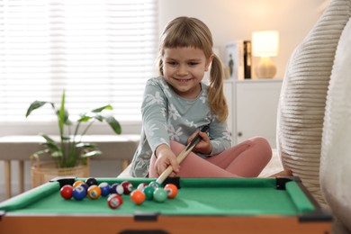 Photo of Cute little girl playing billiards at home