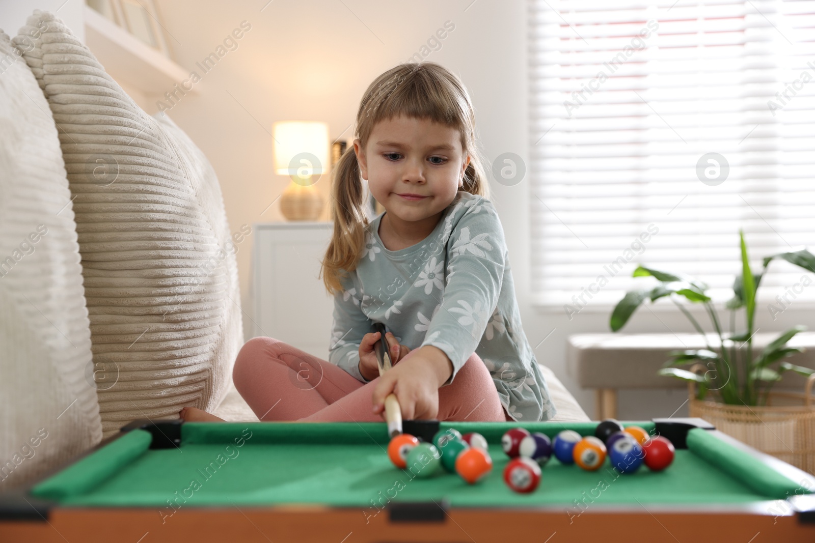 Photo of Cute little girl playing billiards at home