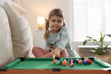 Photo of Cute little girl playing billiards at home