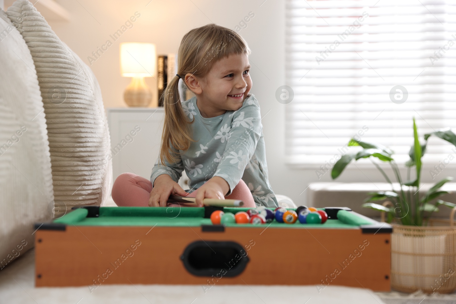 Photo of Cute little girl playing billiards at home