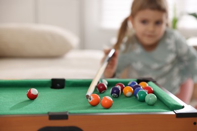 Photo of Cute little girl playing billiards at home, selective focus